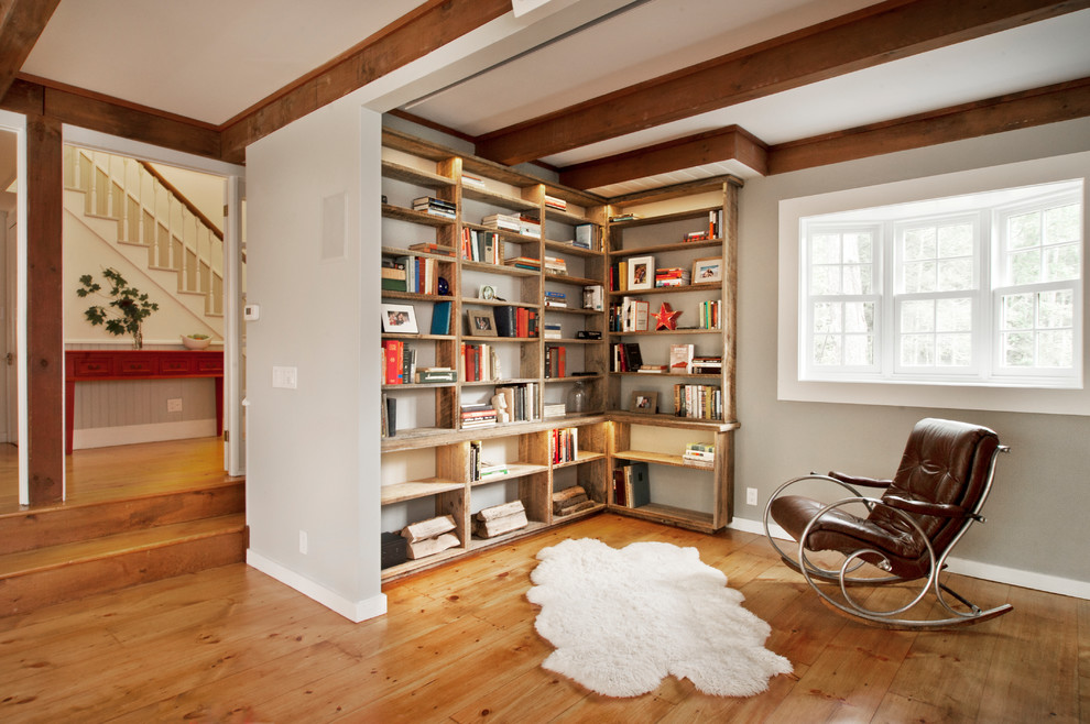 This is an example of a country living room in New York with medium hardwood floors, a library and grey walls.