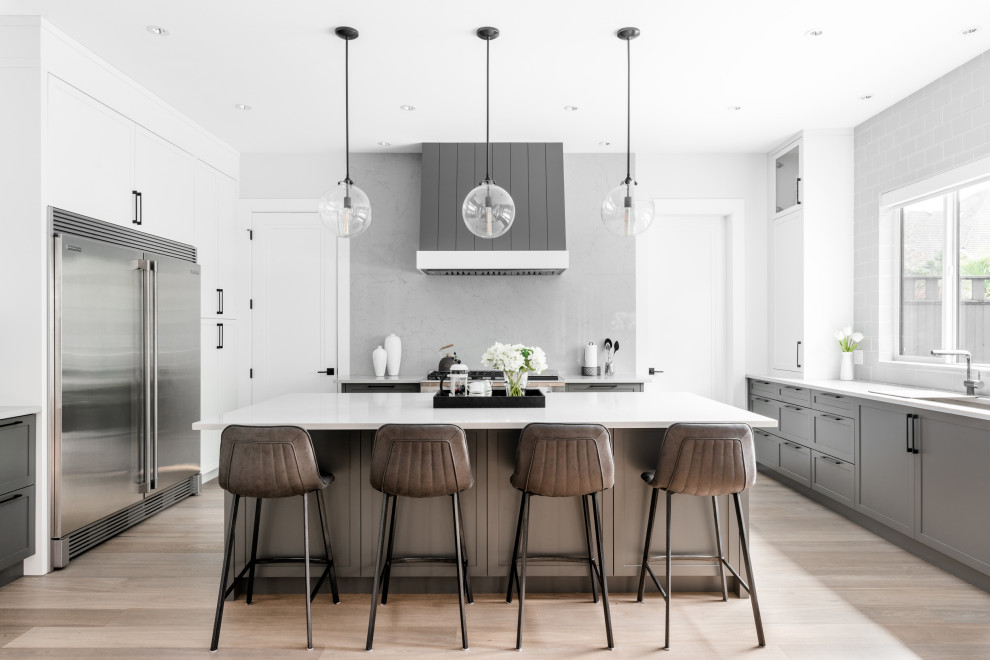 Example of a large transitional u-shaped medium tone wood floor and brown floor open concept kitchen design in Vancouver with an undermount sink, shaker cabinets, gray cabinets, quartz countertops, gray backsplash, stone slab backsplash, stainless steel appliances, an island and gray countertops