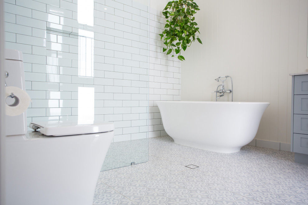 Inspiration for a large contemporary master bathroom in Brisbane with furniture-like cabinets, grey cabinets, a freestanding tub, a corner shower, a one-piece toilet, white tile, white walls, ceramic floors, a drop-in sink, marble benchtops, blue floor and white benchtops.