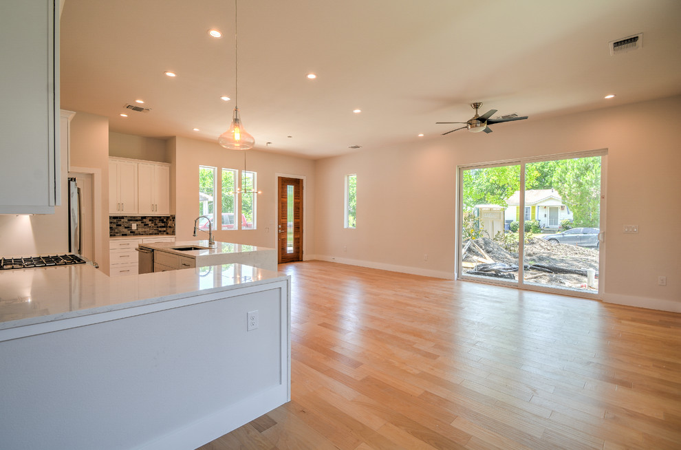 Example of a mid-sized transitional single-wall medium tone wood floor and brown floor open concept kitchen design in Austin with a double-bowl sink, shaker cabinets, white cabinets, marble countertops, gray backsplash, stone tile backsplash, stainless steel appliances, an island and white countertops