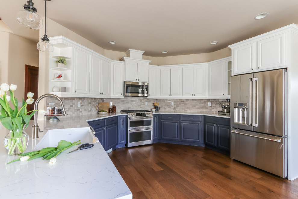Mid-sized transitional u-shaped medium tone wood floor and brown floor kitchen photo in Seattle with a farmhouse sink, white cabinets, quartz countertops, gray backsplash, marble backsplash, stainless steel appliances and white countertops