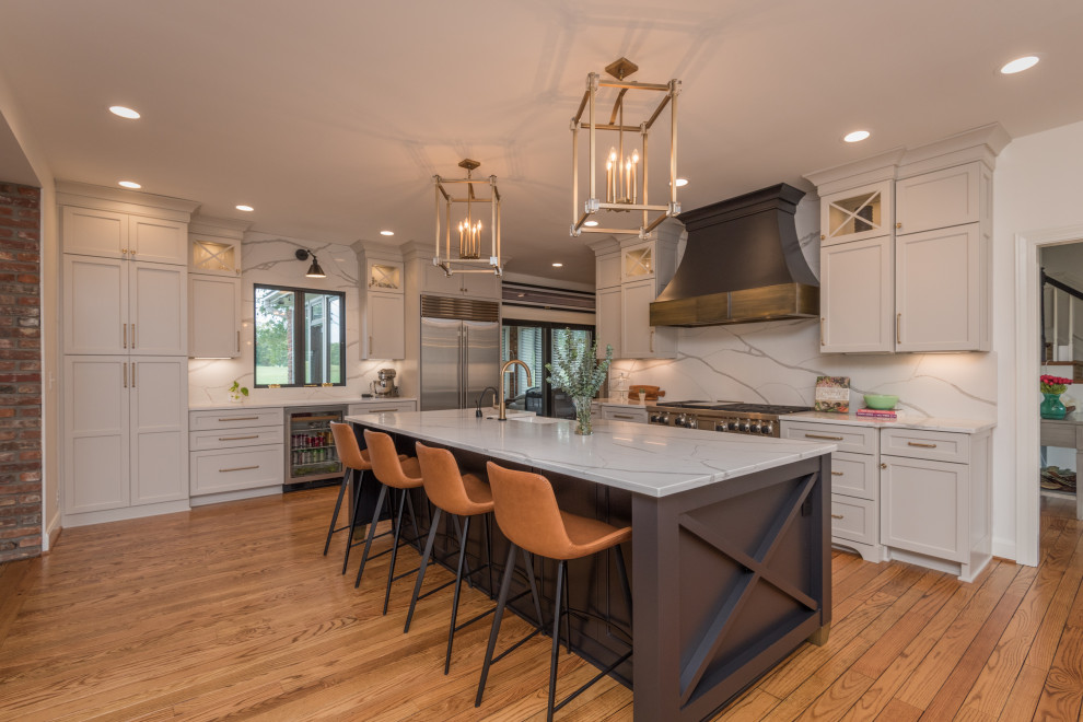This is an example of a large transitional l-shaped kitchen in Louisville with an integrated sink, shaker cabinets, white cabinets, white splashback, stainless steel appliances, medium hardwood floors, with island and white benchtop.