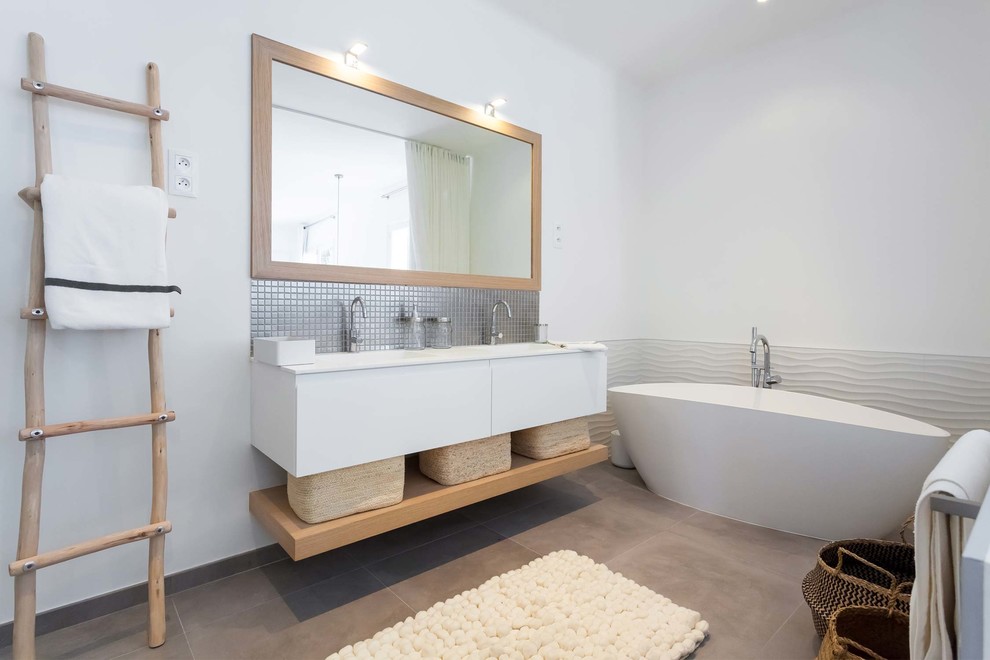 This is an example of a large scandinavian master bathroom in Paris with white cabinets, a curbless shower, white tile, porcelain tile, white walls, ceramic floors, an undermount sink, solid surface benchtops, grey floor, flat-panel cabinets, a freestanding tub and white benchtops.