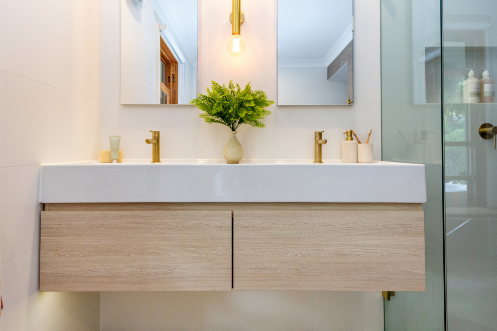 Design ideas for a mid-sized mediterranean 3/4 bathroom in Sydney with flat-panel cabinets, light wood cabinets, a freestanding tub, a corner shower, a two-piece toilet, an integrated sink, a hinged shower door, white benchtops, a niche, a double vanity and a floating vanity.