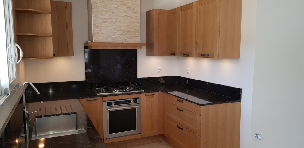 Aménagement de cuisine in bois clair With un évier encastré, un plan de travail en granite, une crédence noire, une crédence en granite, un électroménager en acier inoxydable, un sol en travertin and plan de travail noir.