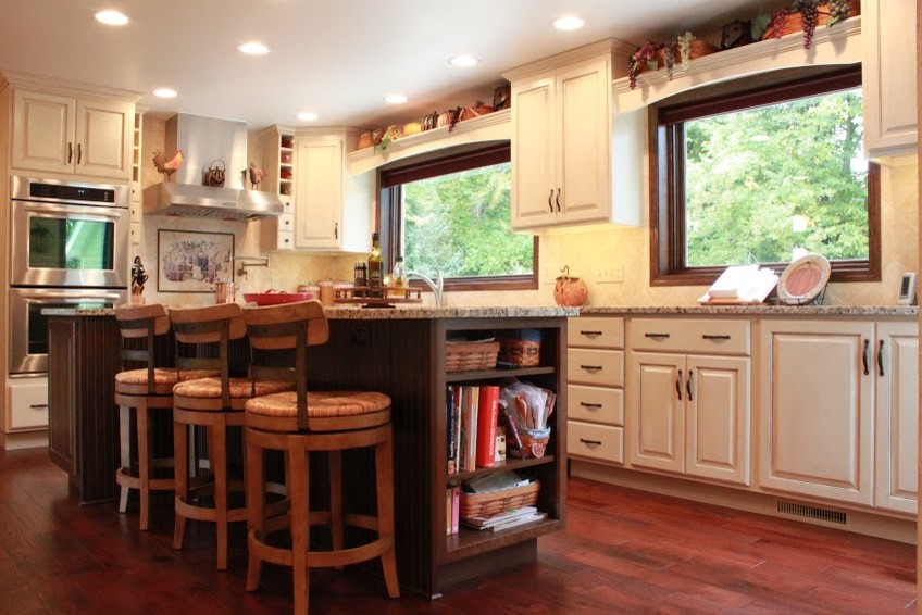 Eat-in kitchen - large modern galley medium tone wood floor eat-in kitchen idea with an undermount sink, raised-panel cabinets, white cabinets, granite countertops, white backsplash, ceramic backsplash, stainless steel appliances and an island