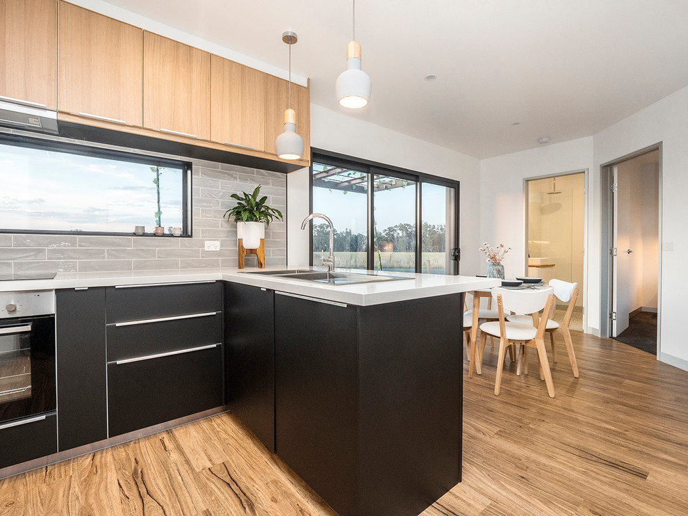 Photo of a small contemporary l-shaped open plan kitchen in Other with black cabinets, grey splashback, ceramic splashback, stainless steel appliances and vinyl floors.