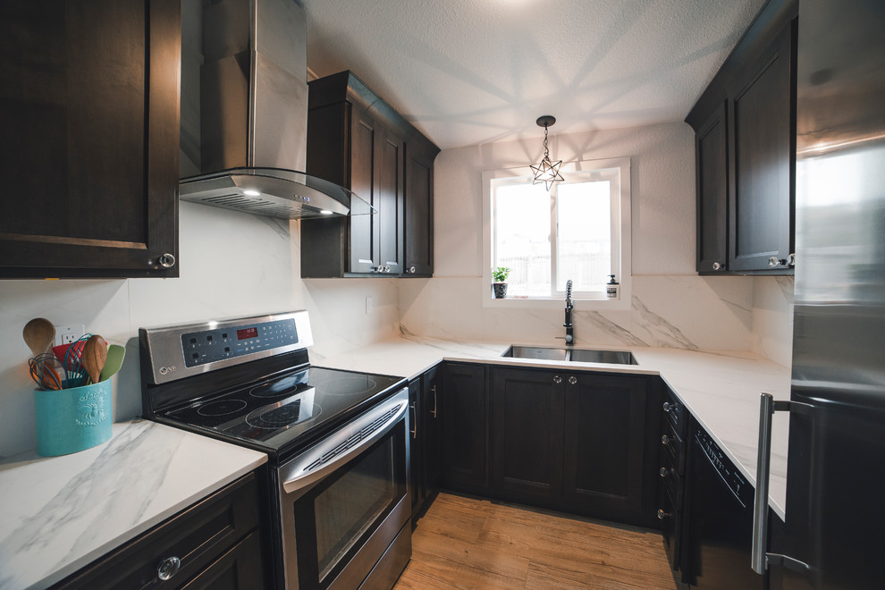 Photo of a small transitional u-shaped separate kitchen in Seattle with an undermount sink, recessed-panel cabinets, dark wood cabinets, quartz benchtops, white splashback, stone slab splashback, stainless steel appliances, vinyl floors, no island, brown floor and white benchtop.