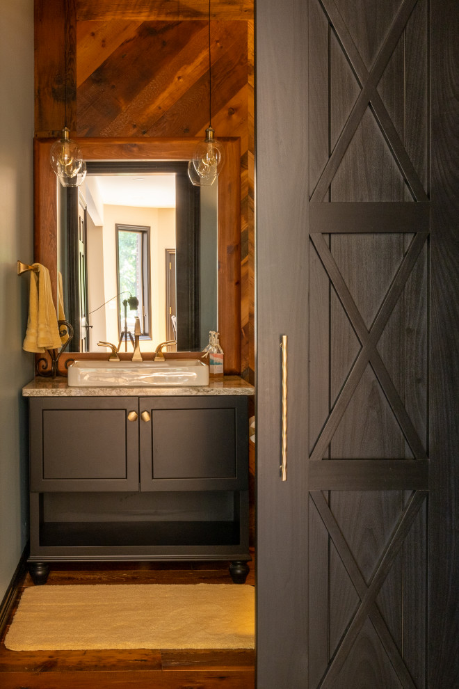 This is an example of a small rustic cloakroom in Detroit with recessed-panel cabinets, black cabinets, a two-piece toilet, brown walls, medium hardwood flooring, a vessel sink, engineered stone worktops, brown floors, grey worktops, a freestanding vanity unit and wood walls.