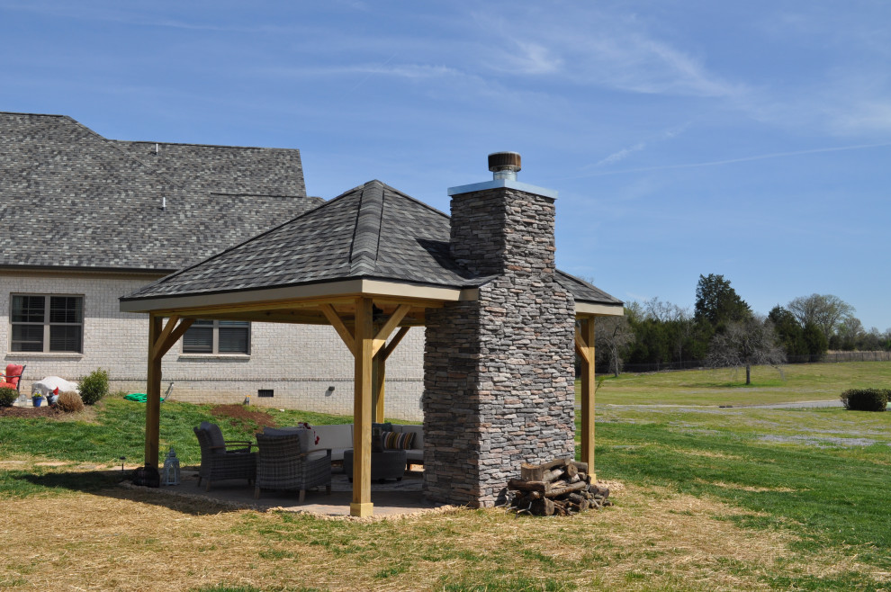Ejemplo de terraza rural en patio trasero con chimenea y adoquines de hormigón