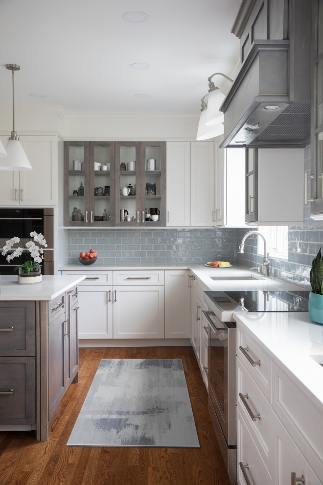 Enclosed kitchen - mid-sized transitional l-shaped medium tone wood floor and brown floor enclosed kitchen idea with an undermount sink, shaker cabinets, white cabinets, quartz countertops, blue backsplash, subway tile backsplash, stainless steel appliances, an island and white countertops