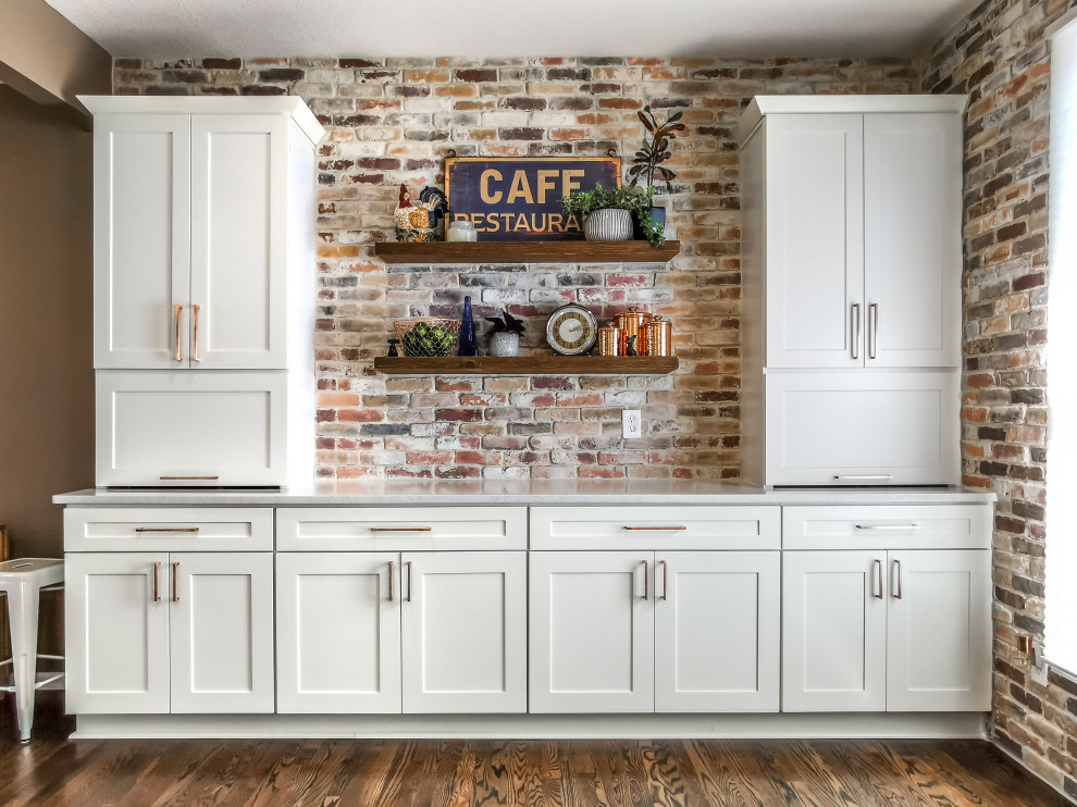 Inspiration for a large country u-shaped eat-in kitchen in Kansas City with a farmhouse sink, shaker cabinets, white cabinets, quartz benchtops, red splashback, brick splashback, stainless steel appliances, dark hardwood floors, a peninsula, brown floor and white benchtop.