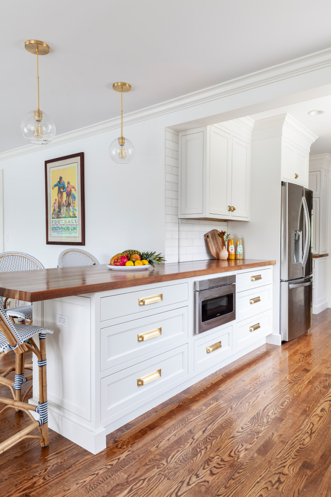 Eat-in kitchen - large eclectic galley medium tone wood floor and brown floor eat-in kitchen idea in Chicago with a farmhouse sink, recessed-panel cabinets, white cabinets, wood countertops, white backsplash, subway tile backsplash, stainless steel appliances, an island and brown countertops