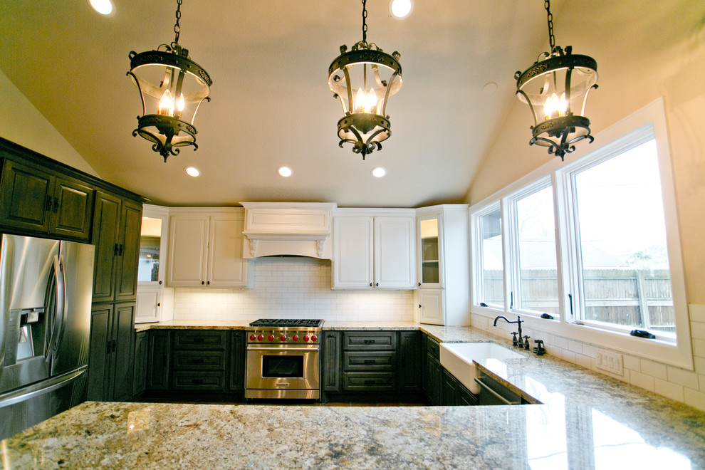 Photo of a large mediterranean u-shaped eat-in kitchen in Houston with a farmhouse sink, raised-panel cabinets, dark wood cabinets, granite benchtops, white splashback, ceramic splashback, stainless steel appliances, terra-cotta floors and a peninsula.