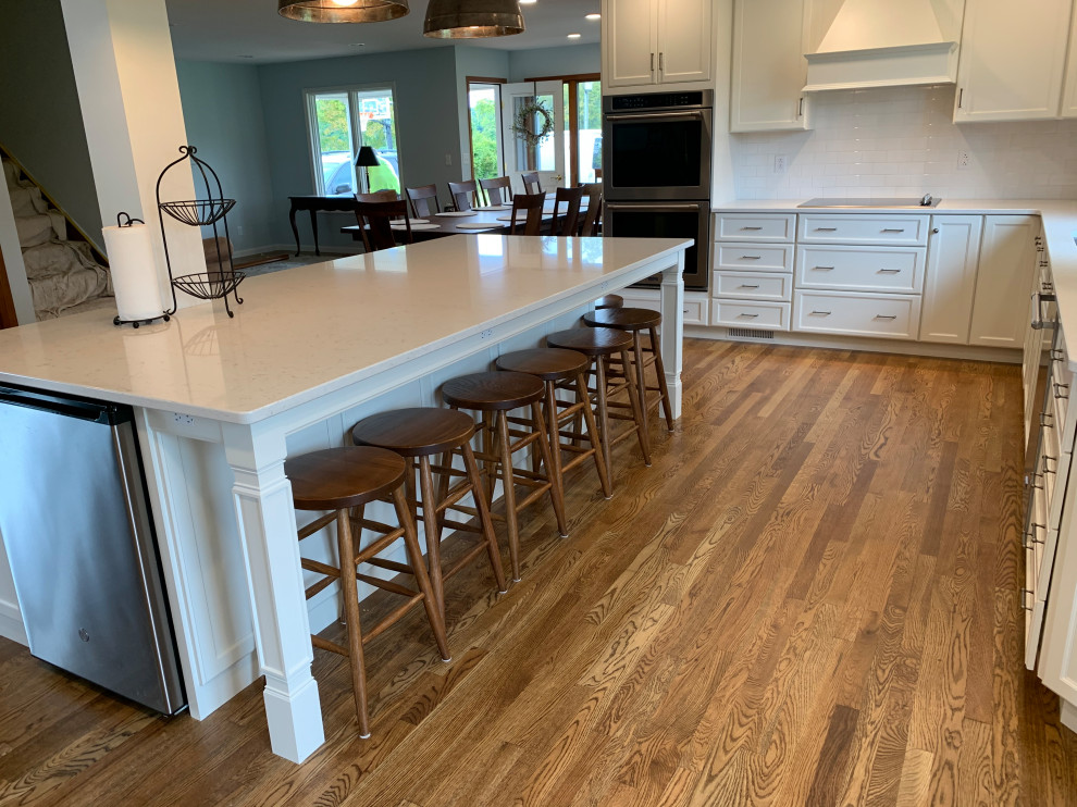Example of a large transitional u-shaped medium tone wood floor and brown floor open concept kitchen design with an undermount sink, recessed-panel cabinets, white cabinets, quartz countertops, white backsplash, stainless steel appliances, an island and white countertops