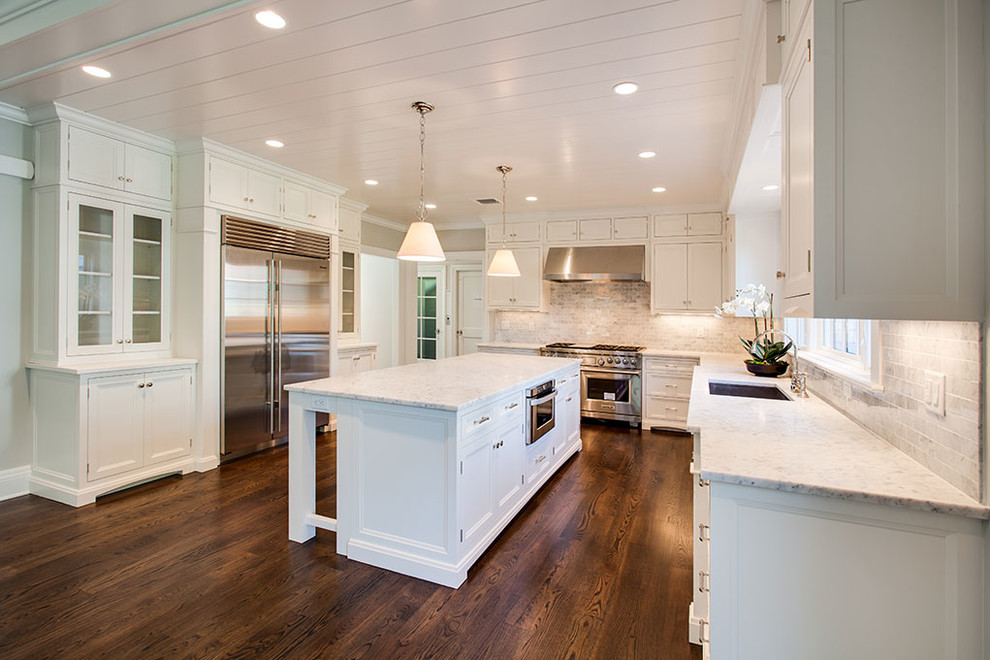 Large transitional u-shaped dark wood floor and brown floor eat-in kitchen photo with an undermount sink, recessed-panel cabinets, white cabinets, white backsplash, stainless steel appliances and an island
