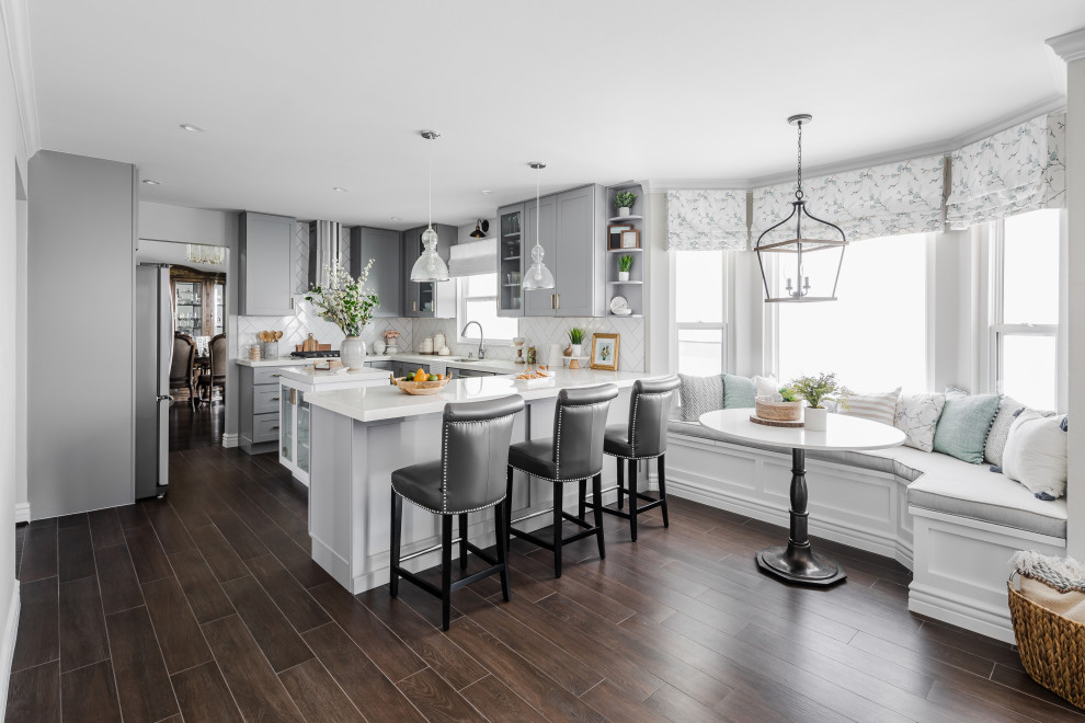Inspiration for a transitional u-shaped dark wood floor and brown floor kitchen remodel in Los Angeles with an undermount sink, shaker cabinets, gray cabinets, white backsplash, stainless steel appliances, an island and white countertops