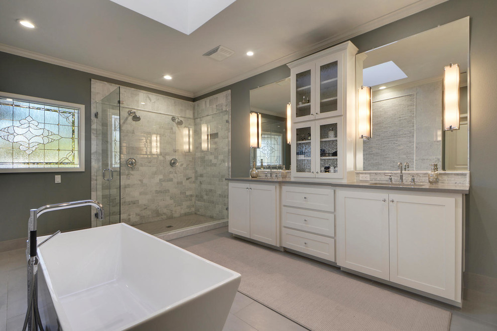 Photo of a large transitional master bathroom in Austin with shaker cabinets, white cabinets, a freestanding tub, a double shower, a one-piece toilet, gray tile, stone tile, grey walls, porcelain floors, quartzite benchtops and an undermount sink.