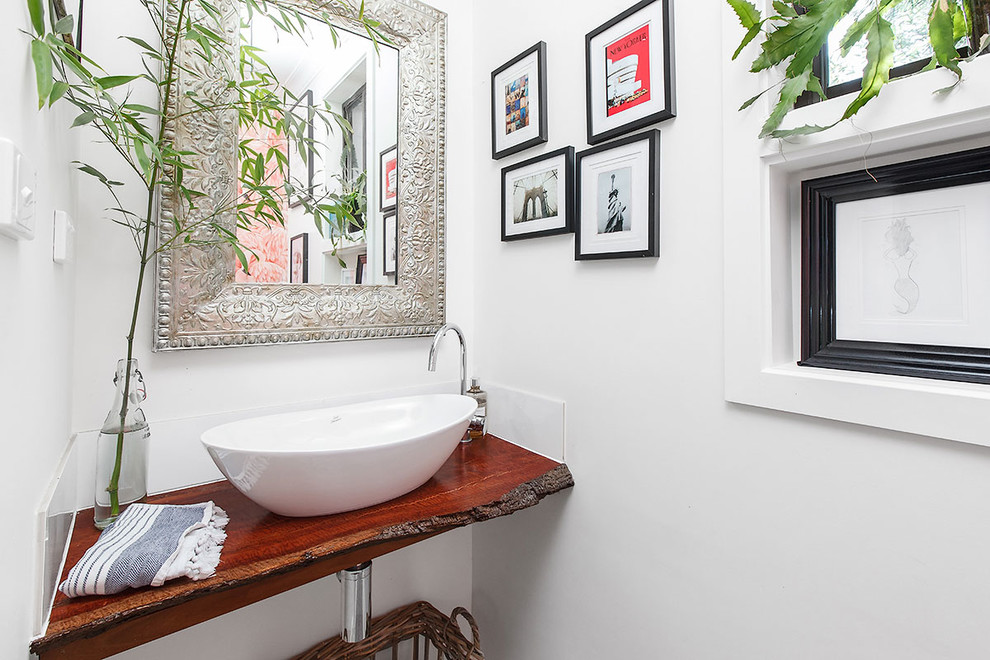 This is an example of a small eclectic powder room in Melbourne with open cabinets, a one-piece toilet, white tile, ceramic tile, white walls, light hardwood floors, a vessel sink, wood benchtops and white floor.