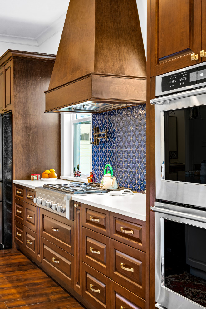 ヒューストンにある高級な広いトラディショナルスタイルのおしゃれなキッチン (アンダーカウンターシンク、レイズドパネル扉のキャビネット、中間色木目調キャビネット、御影石カウンター、青いキッチンパネル、テラコッタタイルのキッチンパネル、シルバーの調理設備、無垢フローリング、茶色い床、青いキッチンカウンター) の写真