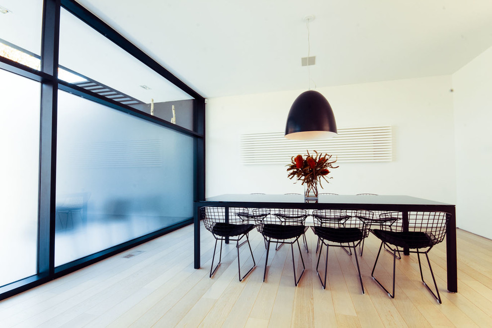 This is an example of a modern dining room in Toronto with white walls and light hardwood floors.