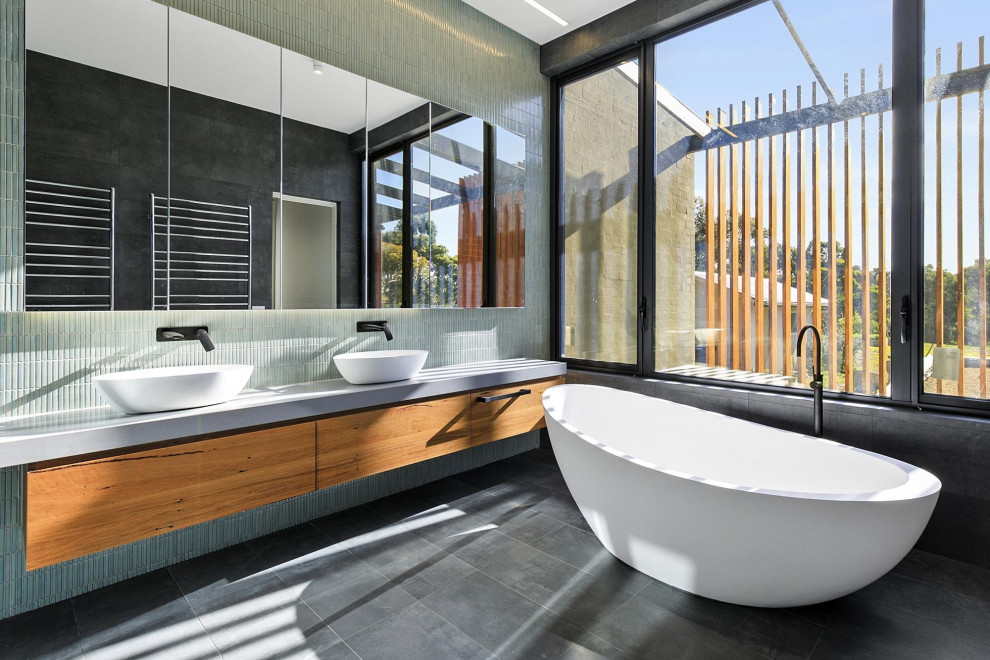 Design ideas for a large industrial master bathroom in Geelong with flat-panel cabinets, medium wood cabinets, a freestanding tub, green tile, mosaic tile, a vessel sink, solid surface benchtops, grey benchtops, a double vanity and a floating vanity.