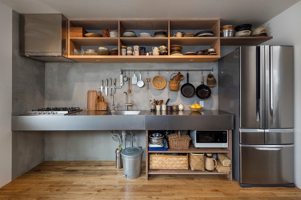 Industrial single-wall kitchen in Tokyo with an integrated sink, open cabinets, stainless steel benchtops, grey splashback, medium hardwood floors and brown floor.