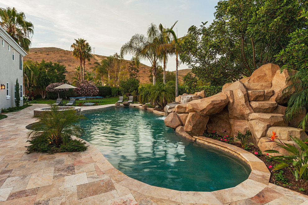 Photo of a large tropical backyard custom-shaped pool in San Diego with natural stone pavers and a water slide.