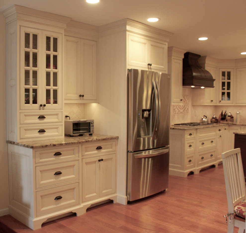 Example of a large classic medium tone wood floor kitchen design with beaded inset cabinets, granite countertops, beige backsplash, stone tile backsplash, stainless steel appliances and an island