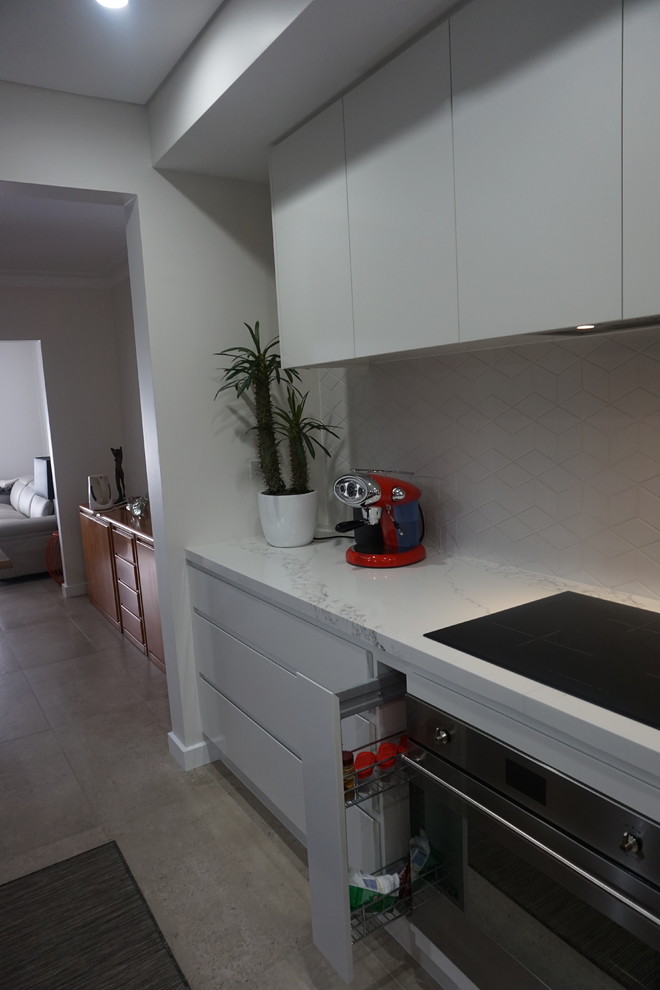 This is an example of a mid-sized contemporary l-shaped eat-in kitchen in Sydney with a drop-in sink, white cabinets, quartz benchtops, white splashback, porcelain splashback, stainless steel appliances, ceramic floors and with island.