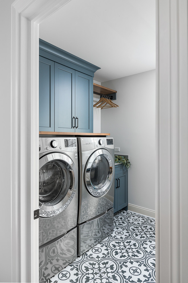 This is an example of a large transitional single-wall utility room in Chicago with white walls, porcelain floors, shaker cabinets, blue cabinets, a side-by-side washer and dryer and multi-coloured floor.