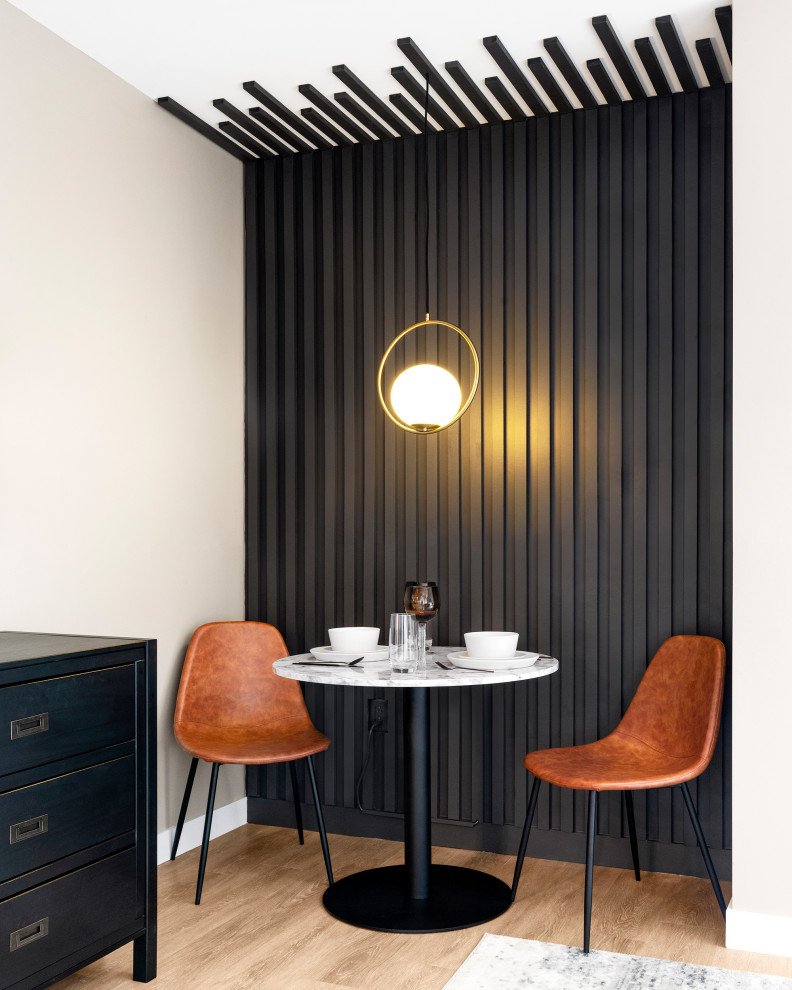 Photo of a small contemporary dining room in New York with banquette seating, black walls, light hardwood flooring, beige floors and wood walls.