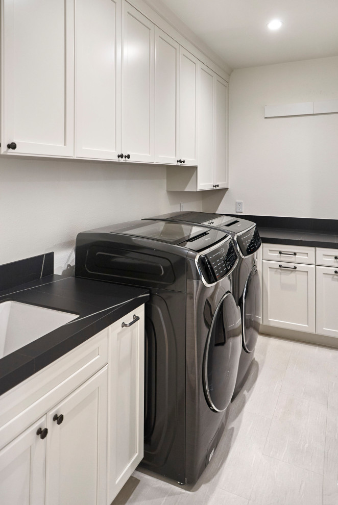Inspiration för stora klassiska l-formade svart tvättstugor enbart för tvätt, med en undermonterad diskho, luckor med infälld panel, vita skåp, bänkskiva i koppar, vitt stänkskydd, stänkskydd i keramik, vita väggar, klinkergolv i porslin, en tvättmaskin och torktumlare bredvid varandra och grått golv
