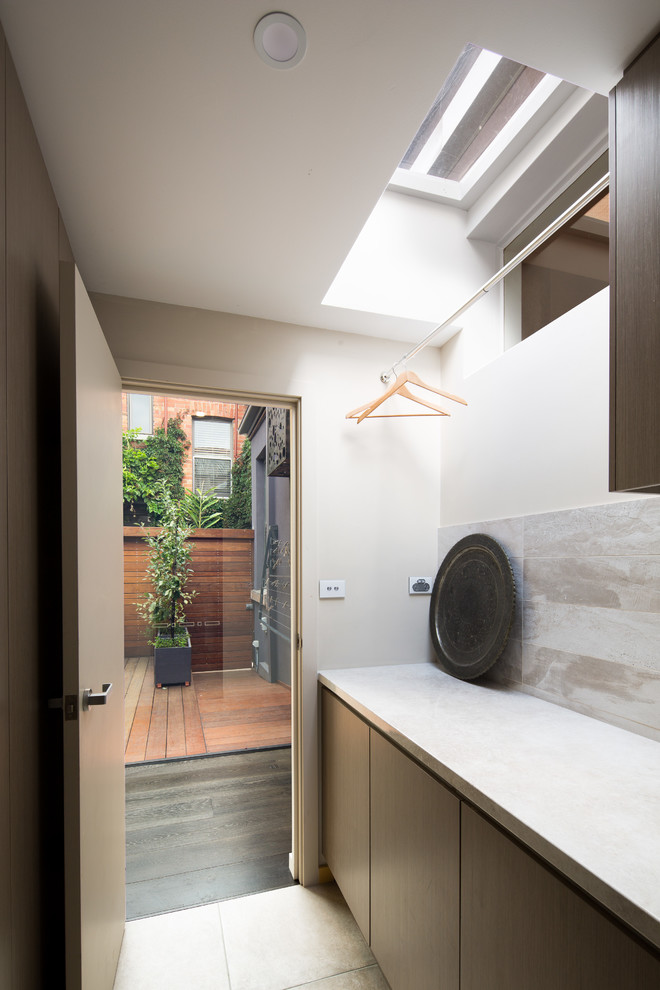 This is an example of a small contemporary single-wall dedicated laundry room in Melbourne with flat-panel cabinets, dark wood cabinets, marble benchtops, white walls, ceramic floors, a stacked washer and dryer, grey floor and white benchtop.