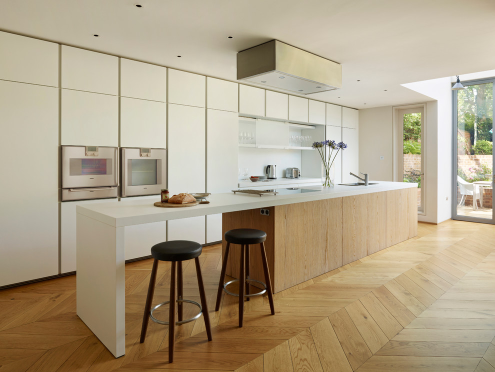 Inspiration for a modern galley kitchen in London with an undermount sink, white splashback, panelled appliances, light hardwood floors, flat-panel cabinets, white cabinets and with island.