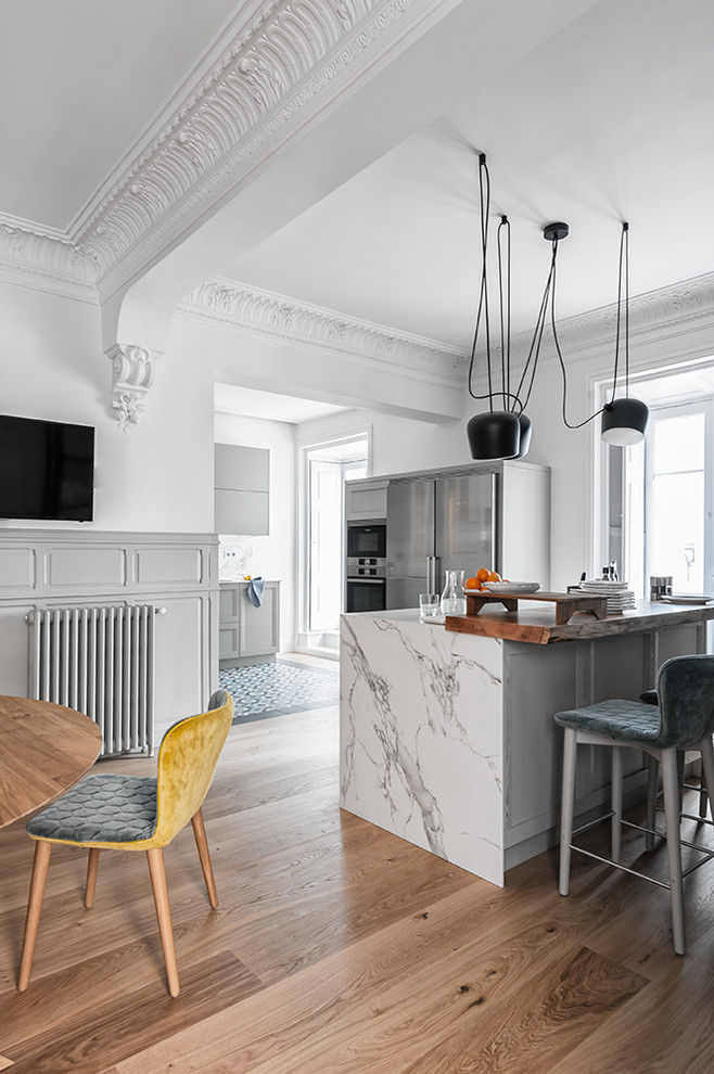 Large contemporary eat-in kitchen in Other with a single-bowl sink, raised-panel cabinets, grey cabinets, marble benchtops, white splashback, marble splashback, stainless steel appliances, light hardwood floors, with island and white benchtop.