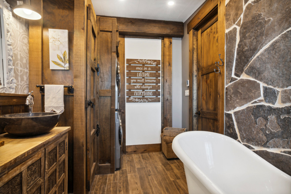 Mid-sized mountain style master ceramic tile, brown floor, single-sink, exposed beam and wainscoting bathroom photo in Other with shaker cabinets, medium tone wood cabinets, wood countertops, a hinged shower door, brown countertops and a freestanding vanity