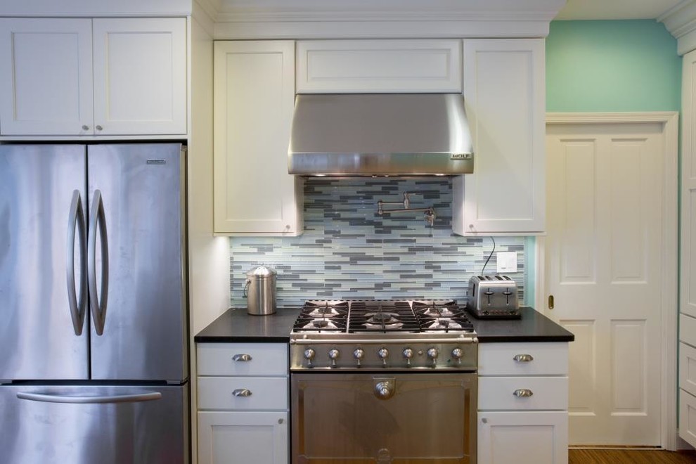 Photo of a country single-wall eat-in kitchen in DC Metro with a farmhouse sink, recessed-panel cabinets, white cabinets, wood benchtops, blue splashback and stainless steel appliances.
