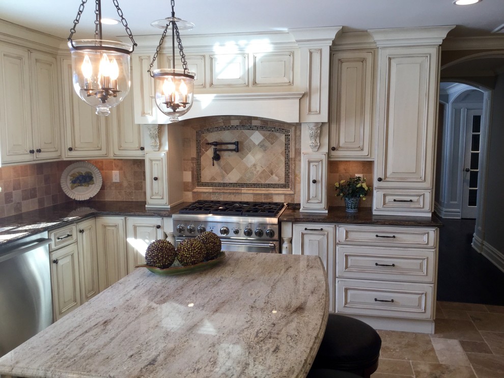 Mid-sized traditional u-shaped eat-in kitchen in Newark with an undermount sink, raised-panel cabinets, granite benchtops, beige splashback, with island, distressed cabinets, stone tile splashback, stainless steel appliances, travertine floors, beige floor and beige benchtop.