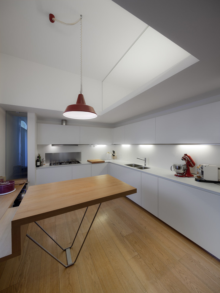 Design ideas for a large contemporary l-shaped eat-in kitchen in Venice with a double-bowl sink, flat-panel cabinets, white cabinets, solid surface benchtops, white splashback and light hardwood floors.