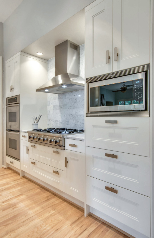 This is an example of a large modern u-shaped eat-in kitchen with a single-bowl sink, shaker cabinets, white cabinets, marble benchtops, white splashback, marble splashback, stainless steel appliances, light hardwood floors, with island, beige floor and white benchtop.