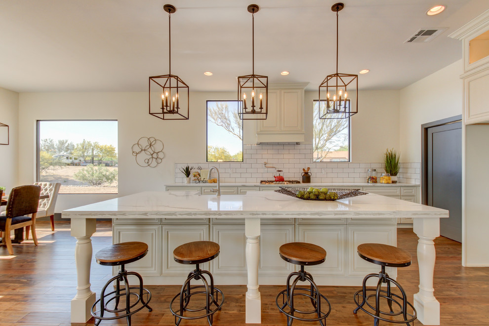 Mid-sized transitional l-shaped dark wood floor and brown floor eat-in kitchen photo in Phoenix with a farmhouse sink, raised-panel cabinets, white cabinets, marble countertops, white backsplash, subway tile backsplash, stainless steel appliances and an island