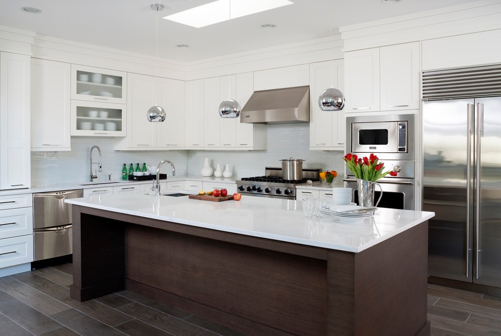 Mid-sized transitional l-shaped ceramic tile and brown floor enclosed kitchen photo in DC Metro with an undermount sink, shaker cabinets, white cabinets, stainless steel appliances, an island, quartz countertops, white backsplash and glass tile backsplash