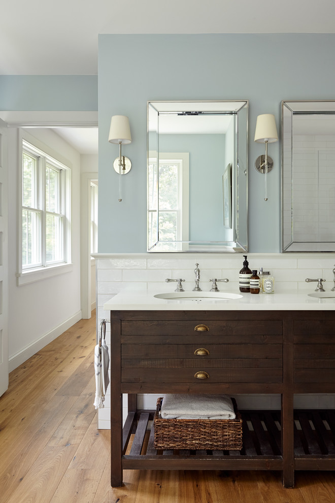 Photo of a mid-sized country master bathroom in Philadelphia with distressed cabinets, a freestanding tub, a two-piece toilet, white tile, ceramic tile, blue walls, light hardwood floors, an undermount sink, marble benchtops, brown floor, a hinged shower door and flat-panel cabinets.