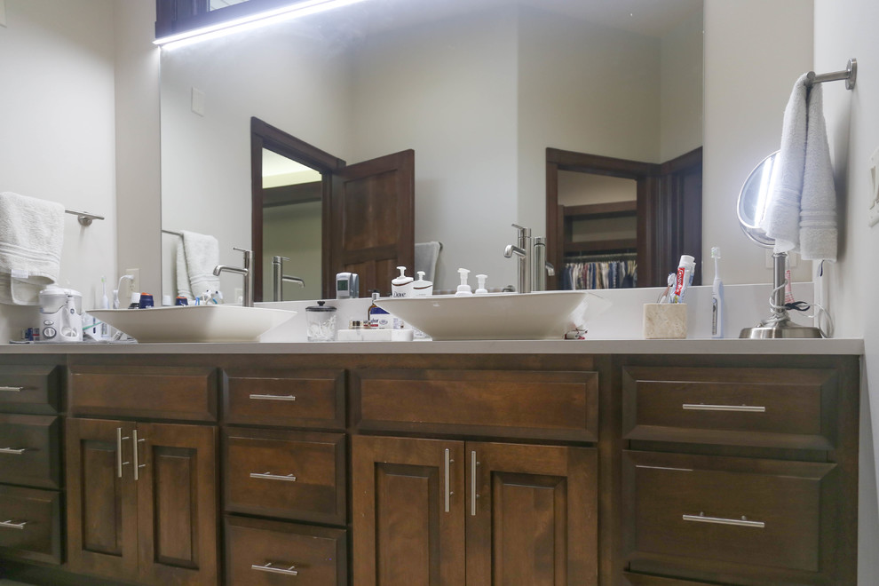 Example of a mid-sized transitional master beige tile and porcelain tile porcelain tile and beige floor alcove shower design with raised-panel cabinets, dark wood cabinets, a two-piece toilet, white walls, a vessel sink, quartzite countertops and a hinged shower door