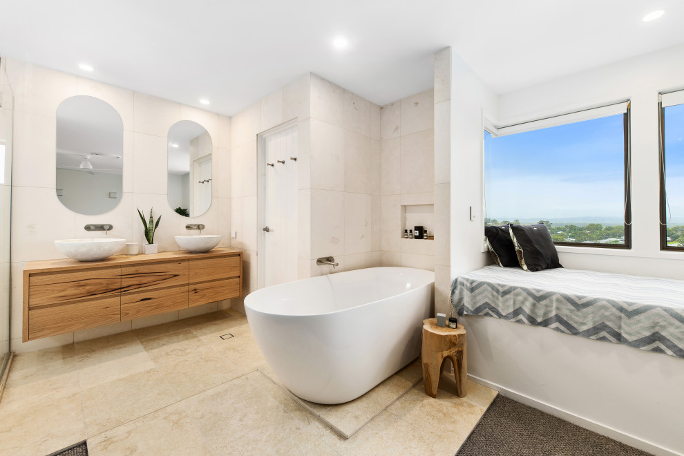 Exemple d'une salle de bain principale bord de mer en bois clair de taille moyenne avec une baignoire indépendante, du carrelage en pierre calcaire, un sol en calcaire, des toilettes cachées, meuble double vasque et meuble-lavabo suspendu.