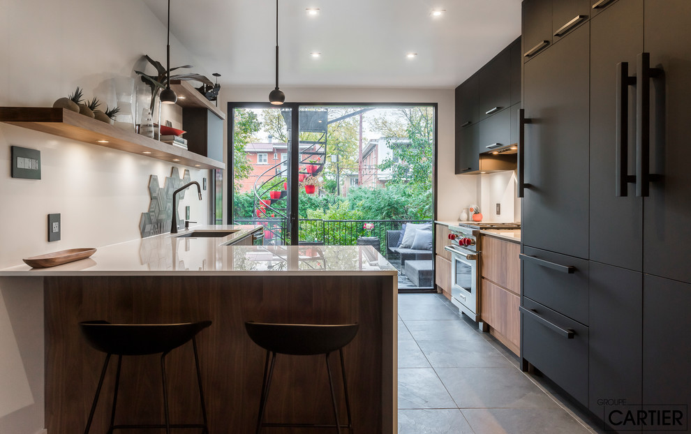 Open concept kitchen - mid-sized modern galley slate floor and black floor open concept kitchen idea in Montreal with an undermount sink, flat-panel cabinets, black cabinets, solid surface countertops, gray backsplash, ceramic backsplash, stainless steel appliances and a peninsula
