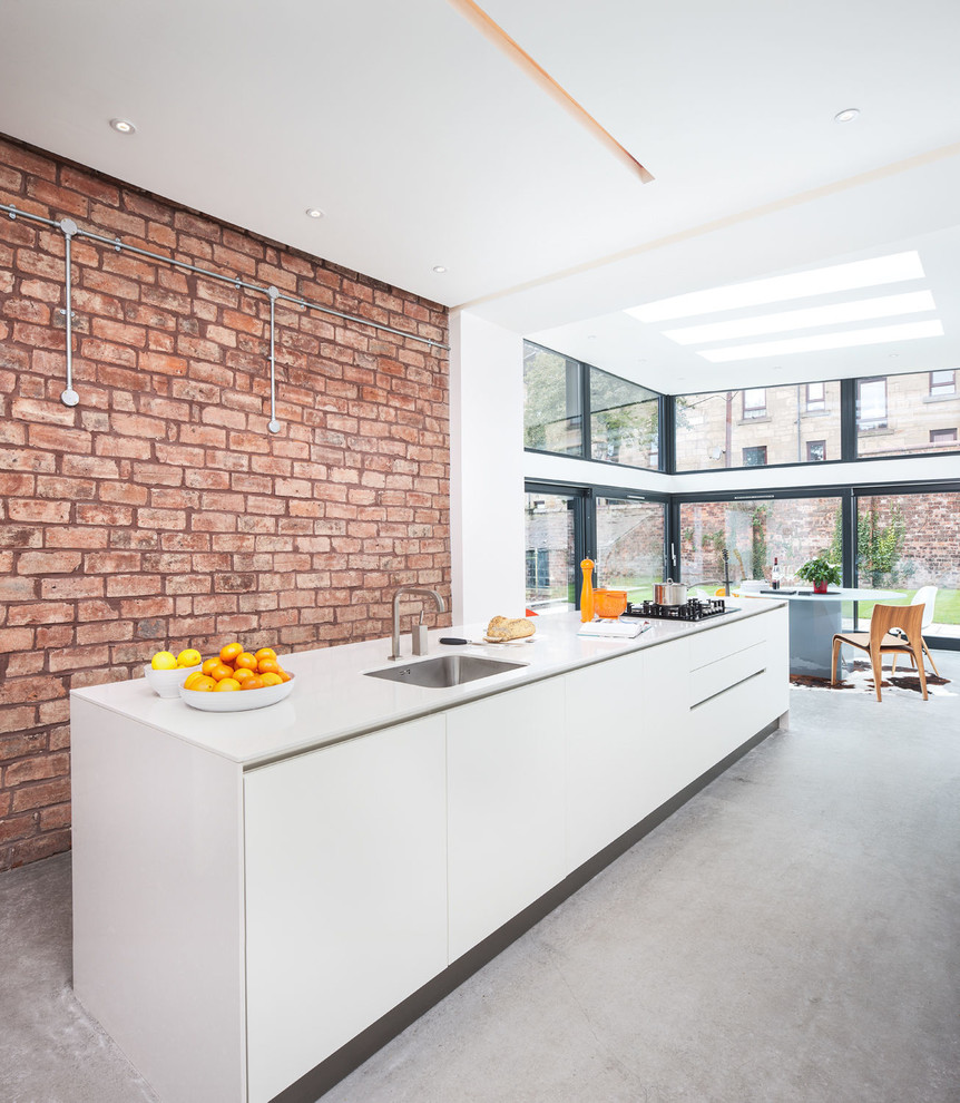 This is an example of a large modern galley eat-in kitchen in Glasgow with a single-bowl sink, flat-panel cabinets, white cabinets, orange splashback, stainless steel appliances, concrete floors and with island.