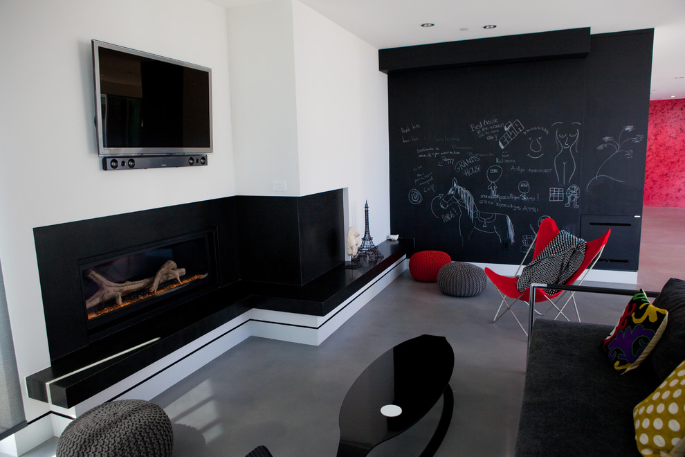 Photo of a contemporary family room in Orange County with black walls, concrete floors, a ribbon fireplace and a wall-mounted tv.
