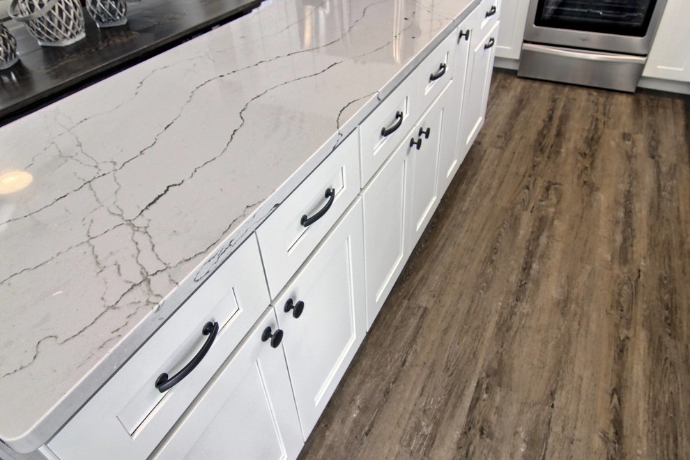 Eat-in kitchen - mid-sized transitional l-shaped vinyl floor eat-in kitchen idea with a farmhouse sink, shaker cabinets, white cabinets, quartz countertops, white backsplash, stone tile backsplash, stainless steel appliances and an island